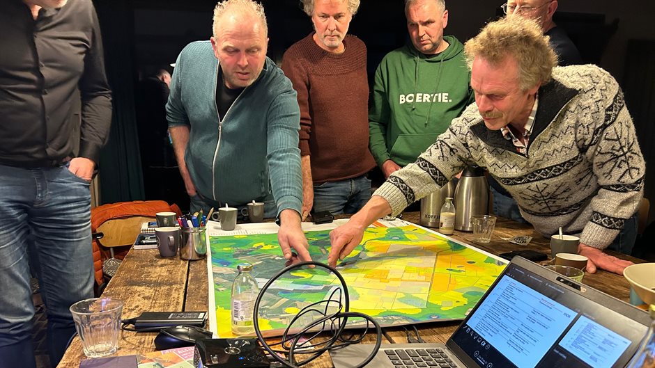 zes mannen wijzen een punt aan op een landschapskaart tijdens een bijeenkomst
